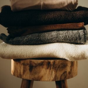 Pile de pulls en maille dans des tons sombres sur un tabouret en bois