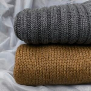 Pulls en maille gris et kaki pliés sur un drap clair