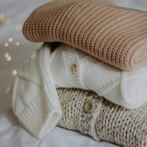 Pulls en maille écrue empilés sur une étoffe blanche